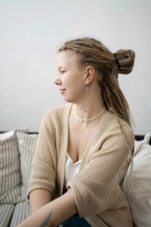 A young woman with dreadlocks and stylish earrings sits on a comfortable sofa She is wearing a