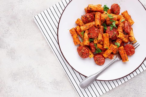Rigatoni pasta with spicy sausage, and rich tomato sauce served, on a white plate, homemade
