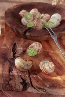 Snails cooked with herb oil on a wooden plate, served with white wine, natural light, no people