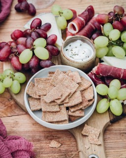An inviting snack platter featuring crisp crackers, juicy grapes, cured meats, and a creamy dip.