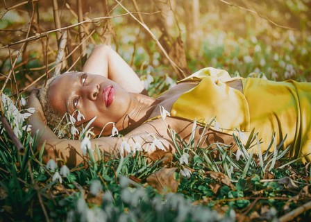 A woman in a golden dress lies peacefully among blooming snowdrops, basking in sunlight in Tacony