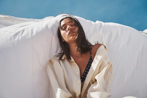 A woman enjoys a sunny summer day on the rooftop, wearing a casual shirt over a swimsuit Her serene