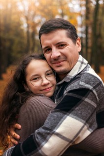 A heartwarming portrait of a father and daughter embracing in a scenic autumn forest. Golden leaves