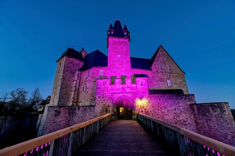 A castle illuminated by pink light at dusk with a bridge in front of it, Spangenberg Castle