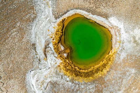 Top view, this drone-captured image shows a striking green lagoon encircled by yellow mineral