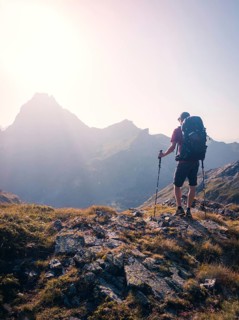 A person stands atop a rocky mountain path at sunrise, holding trekking poles in the Pyrenees. The
