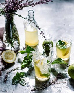 Two glass of lemonade with mint leaves and lemon slices splashes on a table. A bottle of lemonade