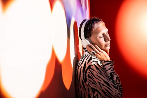 A young, trendy woman wearing oversized headphones enjoying music. She stands against a colorful