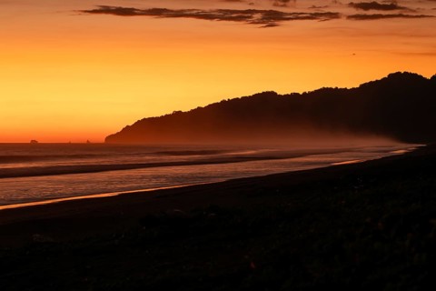 After sunset, the deep red sky glows above palms and ocean spray with views of Corcovado National