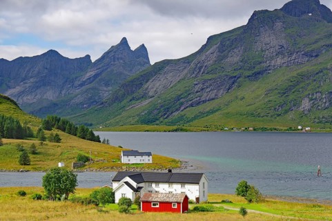 An idyllic valley with houses surrounded by high mountains under cloudy skies, Lofoten, Nordland,