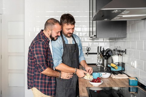 A loving gay couple sharing a joyful moment while preparing a meal in a modern kitchen. They are