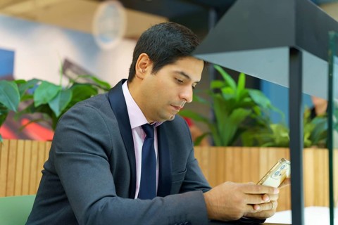 A young Chilean businessman in formal attire sits in a modern environment, focused on his