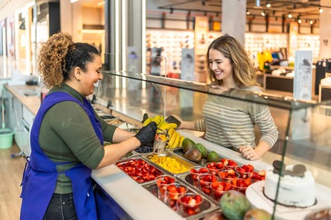 Smiling shop assistant working at a healthy fruit stand in a shopping mall, preparing a delicious,