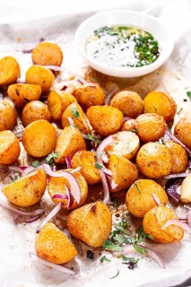 Roasted potatoes sit on a baking sheet next to chopped herbs and red onions. They are golden brown