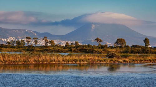 A mountain covered with clouds in the background, surrounded by water and trees, Gialova lagoon,