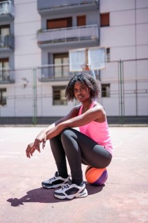 Vertical portrait of an African american woman looking at camera sitting on basketball ball