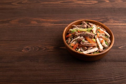 Meat salad with beef and vegetables in wooden bowl on brown wooden background. side view, copy