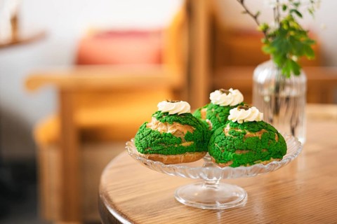 Three green matcha choux pastries topped with whipped cream served on a glass platter of the cafe.