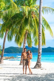 Couple embracing on beautiful white sand beach with turquoise water and palm trees on malcapuya