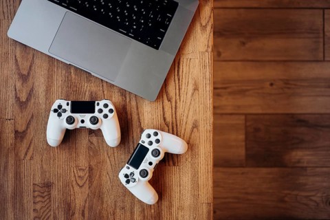 A gaming setup featuring a laptop and two white controllers on a wooden desk. The image captures