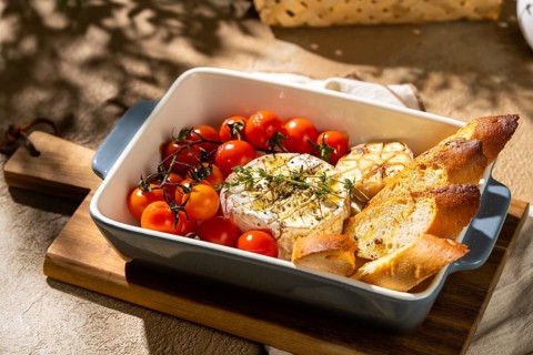 Savory baked Camembert cheese, garnished with fresh herbs, surrounded by cherry tomatoes and