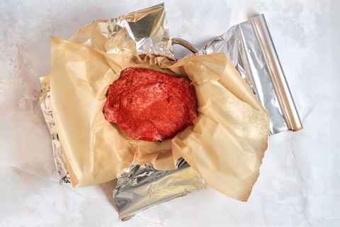 Pork shoulder is placed in a baking pan wrapped in parchment paper and aluminum foil. The setup