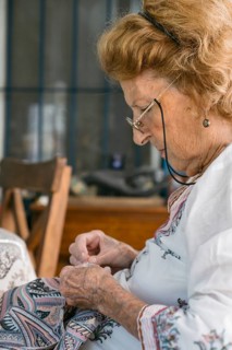 Focused elderly seamstress meticulously sewing fabric with needle and thread, demonstrating