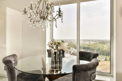 A sophisticated dining area features a round glass table with plush chairs, a stylish chandelier,
