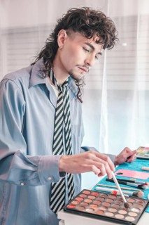 Young make-up artist carefully selecting shade from eyeshadow palette with brush, preparing for