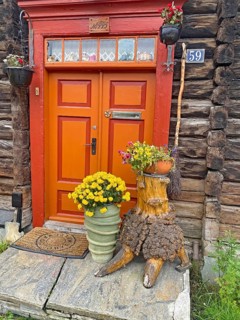 An orange wooden door with decorative flower pots and a wooden sculpture in front of a rustic