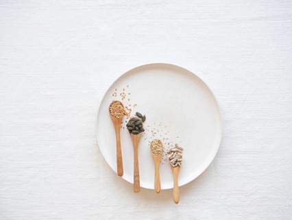 Wooden spoons holding flaxseed, pumpkin, sesame, sunflower seeds, and capsules on a plate