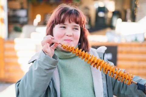 A girl enjoys a crispy spiral tornado potato at an outdoor market. The fun snack on a stick is