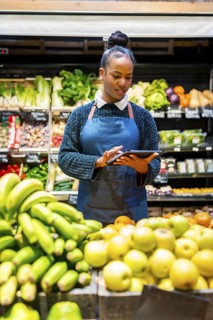 Grocery store employee managing fresh produce inventory with a digital tablet, ensuring quality and