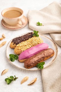 Set of eclair, traditional french dessert and cup of coffee on gray concrete background and linen