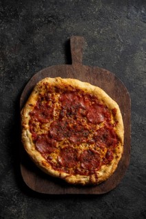 A mouthwatering homemade pepperoni pizza rests on a rustic wooden board against a textured dark