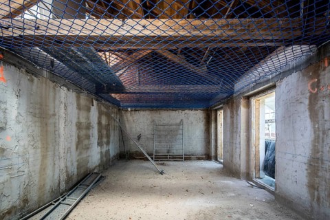 Interior view of a construction site featuring concrete walls, exposed beams, and safety netting.