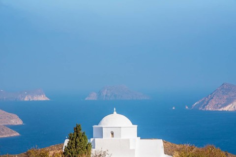 A beautiful white church with a dome overlooks the calm blue sea and distant islands on Milos,