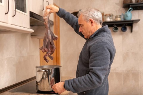 A man carefully prepares octopus in a modern kitchen. He holds the tentacled creature above a