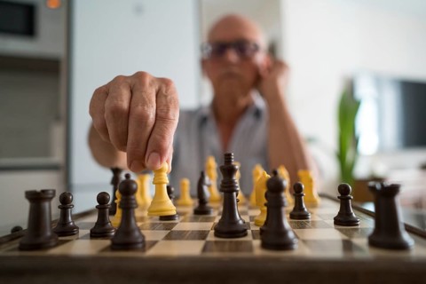 A senior man is deeply focused on a chess game at home, moving a piece thoughtfully. This intimate
