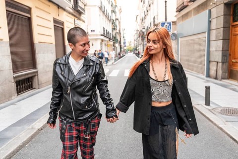 A lesbian couple joyfully holds hands while strolling down a lively urban street, surrounded by