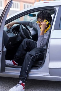 Trendy african boy using phone sitting inside a car