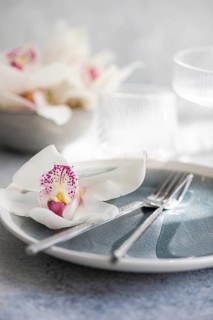 A sophisticated dining setup featuring a white orchid on a blue gray plate, complemented by