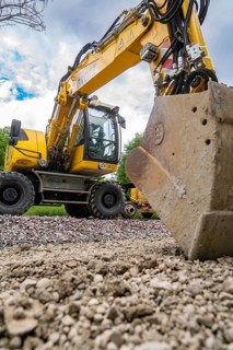 Large yellow excavator on a construction site with a shovel in the foreground and a cloudy sky in