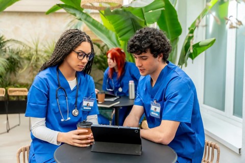 Group of diverse medical students wearing blue scrubs discussing academic material and