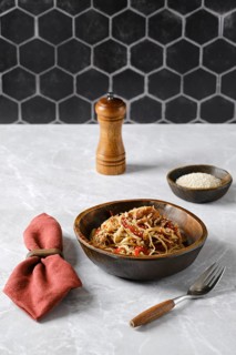 An appetizing plate of pasta with pulled beef in a rustic brown bowl, garnished with vegetables and