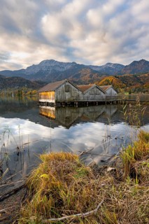 Boathouses in the lake at sunrise, Lake Kochel in autumn with reflection, behind mountain peaks
