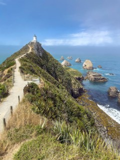 Nugget Point Lighthouse with Nugget Rocks in front of a blue sky, South Island, New Zealand,