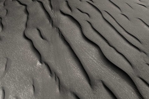 A detailed view of undulating black sand patterns left naturally sculpted by wind and water,