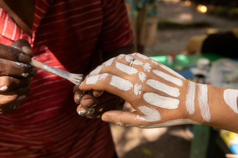 A person paints intricate white patterns on another's hand, capturing the cultural essence of