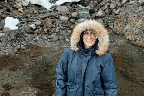 A woman smiles warmly while wearing a fur-lined winter coat in the rocky terrain of Astun, a